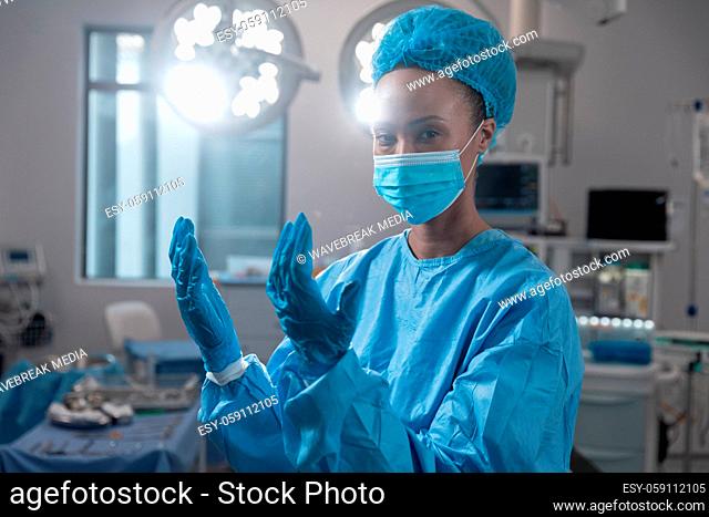 Mixed race female surgeon wearing face mask and protective clothing in operating theatre
