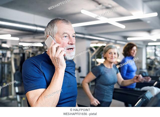 Group of fit seniors working out on treadmills in gym, man with smart phone