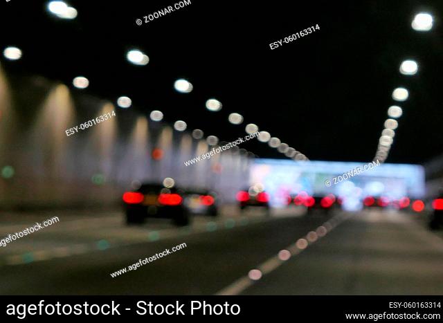 Blurred image of red rear car lights and overhead white lights taken inside road tunnel. High quality photo with copy space