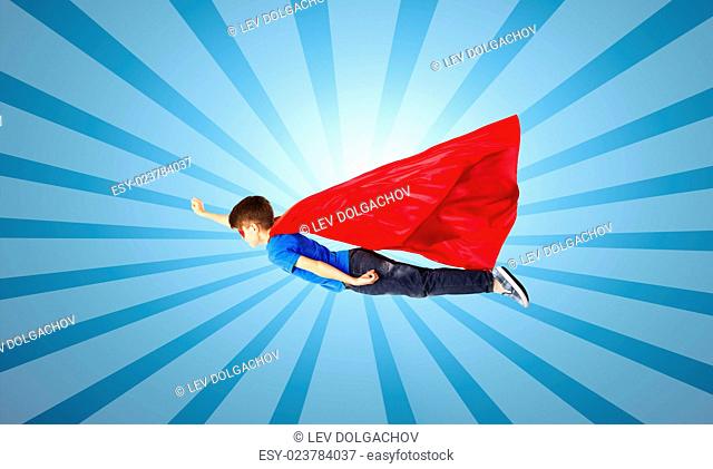 happiness, freedom, childhood, movement and people concept - boy in red superhero cape and mask flying in air over blue burst rays background