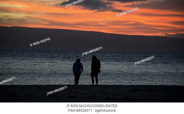 Two unidentified people on the beach at sunset looking towards the Hawaiian island of Lanai from Kaanapali Beach, Maui, Hawaii on Thursday, February 23, 2017
