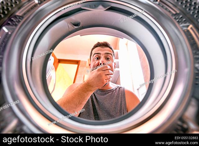 Shocked upset Young man Looking At Stained Bleached Cloth In Washing Machine. View from the inside of washing machine