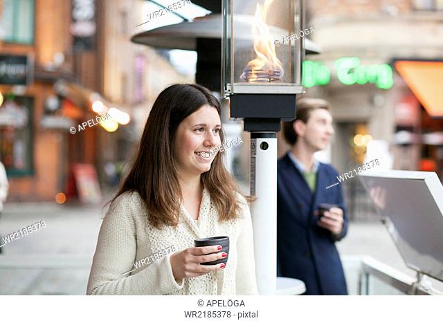 Happy young woman holding coffee cup while man standing at sidewalk cafe