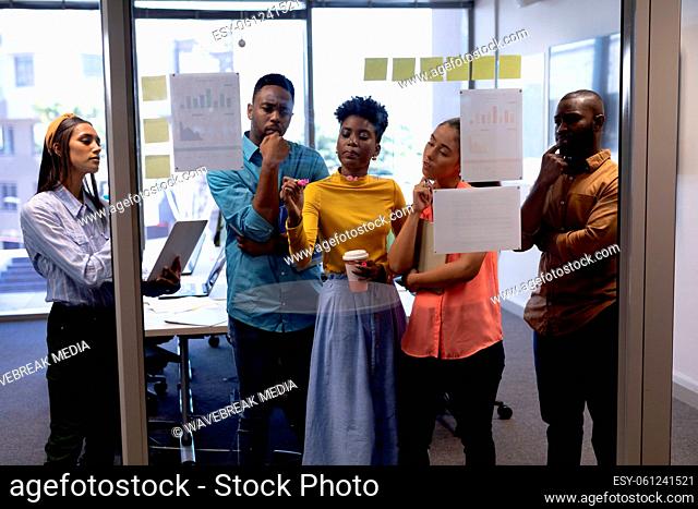 African american businesswoman writing strategy on glass while planning with biracial colleagues