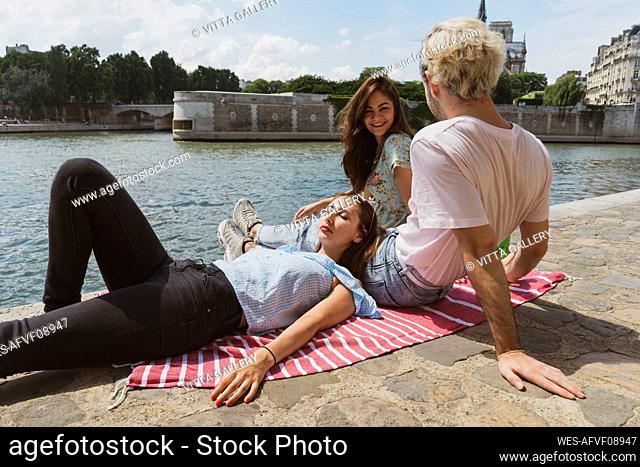 Smiling woman talking with man while female friend sleeping on lap during summer