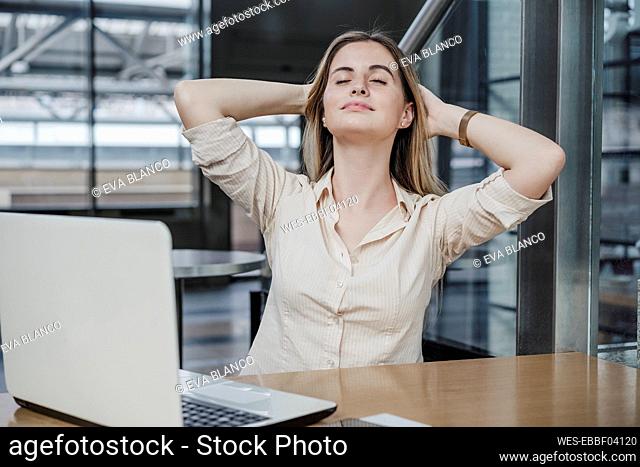 Relaxed businesswoman sitting with hands behind head in cafe
