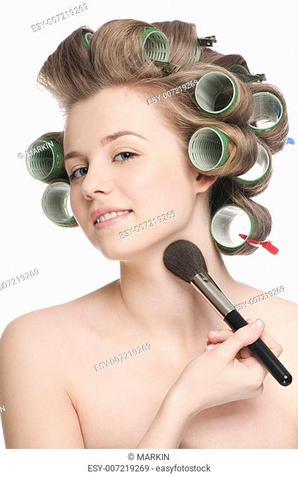Beautiful young adult woman in hair roller applying cosmetic powder brush - close-up portrait
