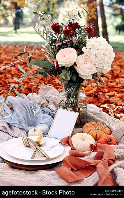 Autumn wedding table setting. Garden party celebration, picnic with golden cutlery, porcelain plate, wine glass and white pumkins