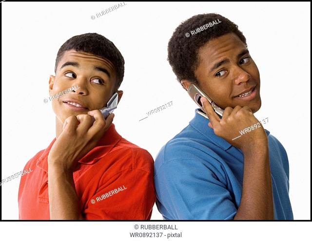 Close-up of two young men standing back to back talking on mobile phones