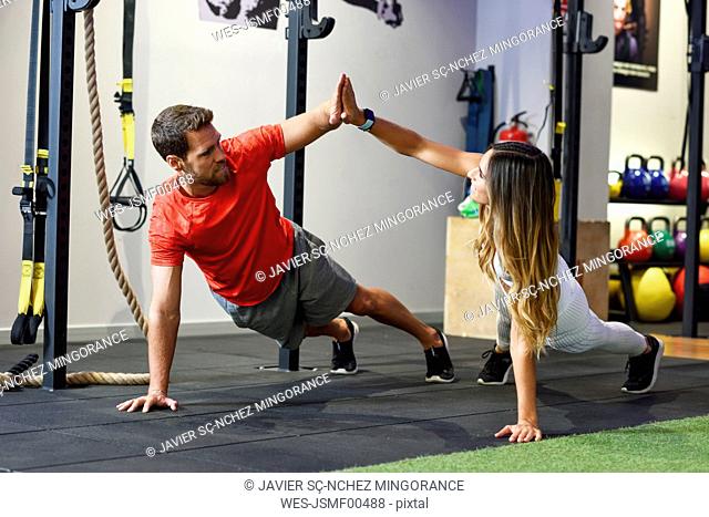Couple exercising side plank with high-five in a gym