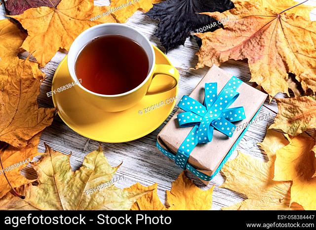 Flat lay autumn composition with gift box and cup of black tea. Time of tea break. Happy thanksgiving congratulation with yellow autumn leaves on vintage wooden...