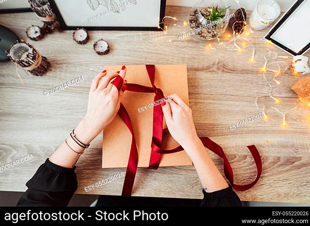Woman's hands wrapping handmade present in paper with red ribbon