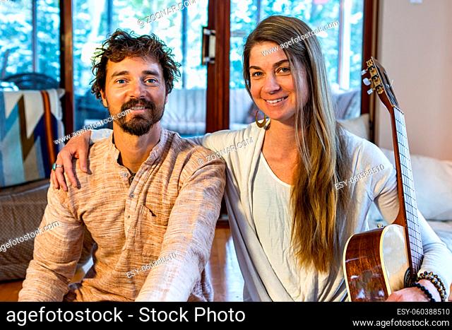 Happy shamanic man and woman in room holding musical instruments like classical guitar looking at camera while preparing for calm peaceful meditation