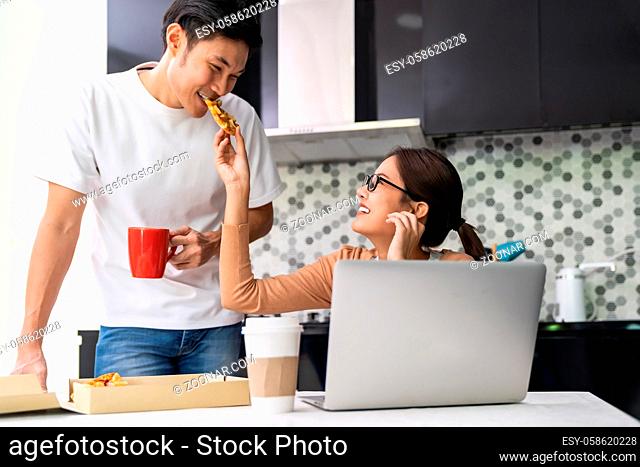 Asian couple work from home in the kitchen and eating delivery pizza take away food and take out coffee while city lockdown from coronavirus covid-19 pandemic