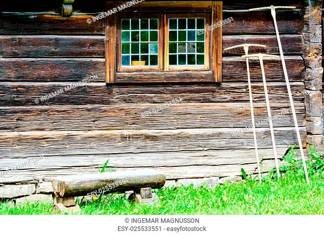 Three rakes beside window leaning against timber wall. Log bench in front of house. Rakes are handmade.