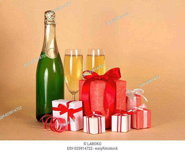 Bottle and wine glasses with champagne, big and small gift boxes on a beige background