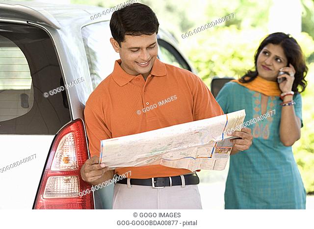 Man reading a road map outside car
