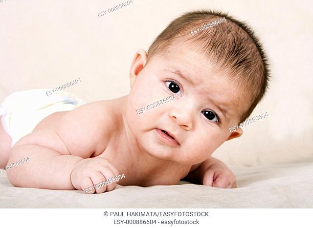 Cute Caucasian Hispanic baby infant laying on belly lifting head making funny expression