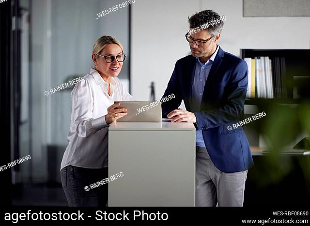 Business colleague discussing over tablet PC at desk in office