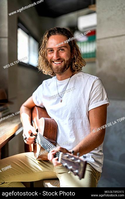 Smiling guitarist playing guitar at home