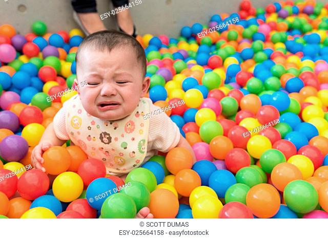 A cute crying girl sitting in a colorful ball pit at a playground