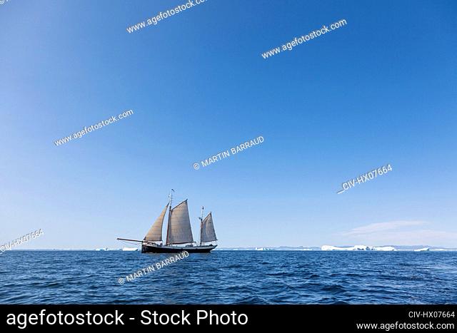 Ship sailing past melting polar ice on sunny blue Atlantic Ocean Greenland