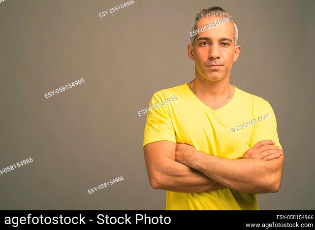 Studio shot of handsome Persian man with gray hair wearing yellow shirt against gray background