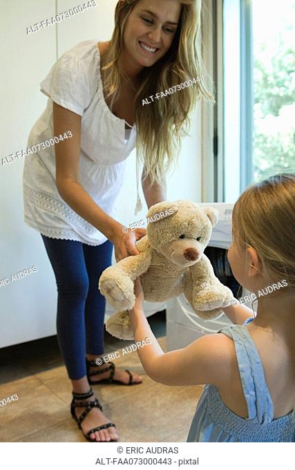Mother handing freshly cleaned teddy bear to little girl