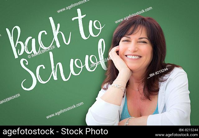 Back to school written on green chalkboard behind smiling middle aged woman