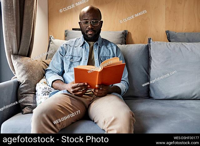 Man reading novel sitting on sofa at home