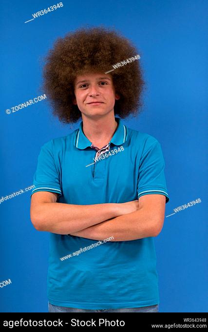 portrait of a young man with a funky hairstyle with arms crossed on blue background