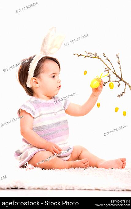 Baby girl in easter bunny costume, playing with yellow easter egg decoration. Isolated on white background