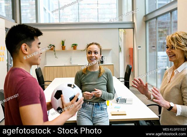 Smiling male and female professionals playing with soccer ball at coworking office