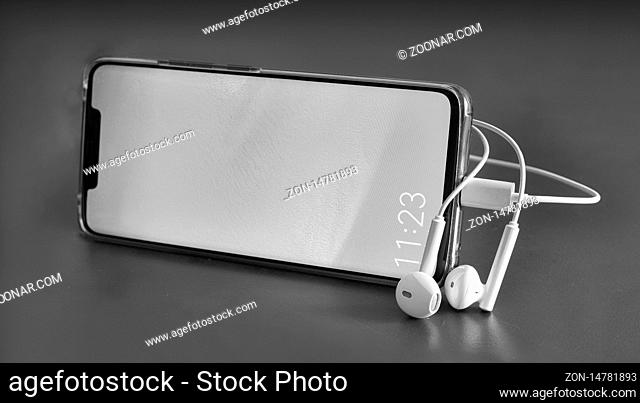 Modern smartphone and headphones, black and white image. Close-up, front view, copy space