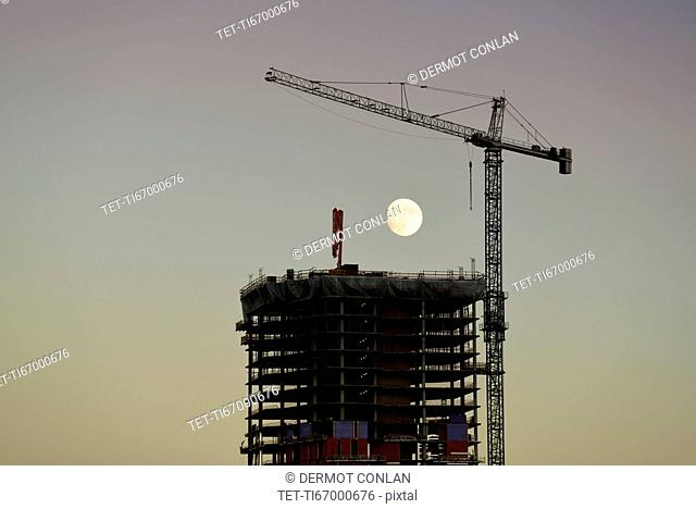 USA, Colorado, Denver, Full moon in background of skyscraper construction site at dusk