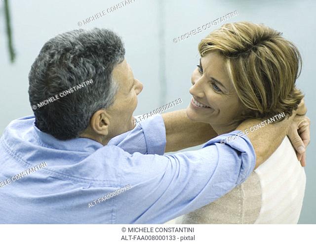 Mature couple smiling at each other, man with arms around woman's neck