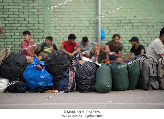Refugees sit behind a line of backpacks and bags used as placeholders for refugees waiting for busses that will allow them to continue their journey