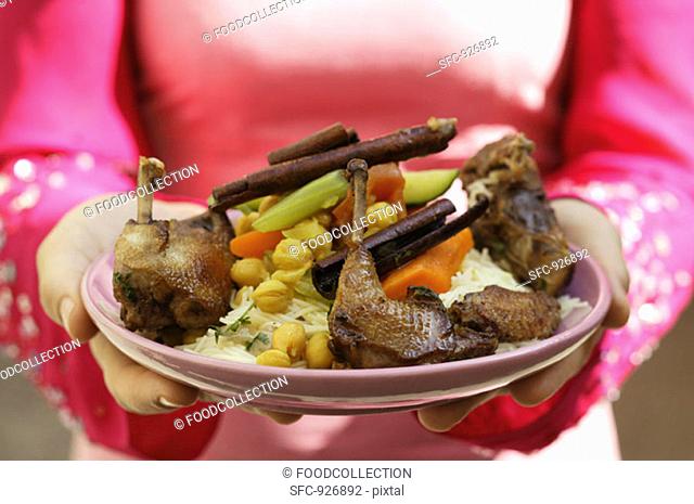 Woman serving roast pigeon with vegetables on noodles Morocco