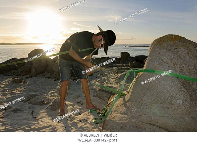 France, Bretagne, Landeda, Man fixing slackline on beach