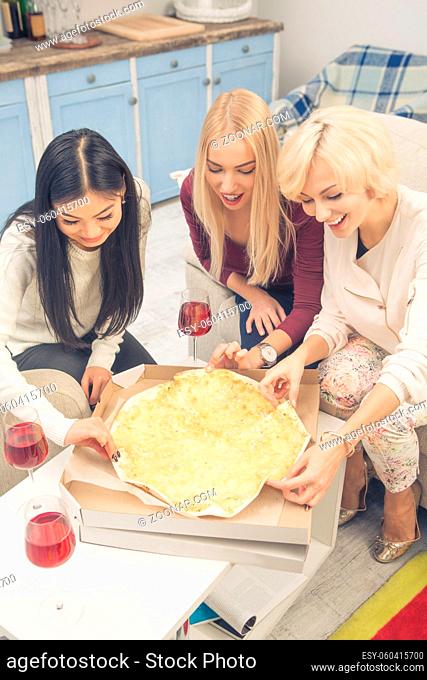 Toned picture of happy beautiful ladies resting and relaxing after hard working day or week. Friends girls having party with delicious pizza with cheese at home