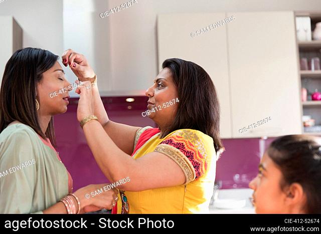 Indian woman placing bind on forehead of sister