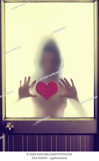 A woman behind frosted-glass door touching a heart shaped cut-out