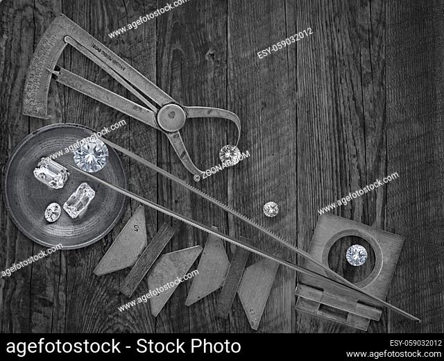 black and white image of a vintage jeweler tools and diamonds over wooden bench, space for text