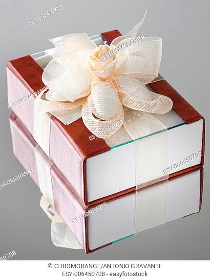 The gift box with a brown cover is wrapped up by a beige tape with a bow