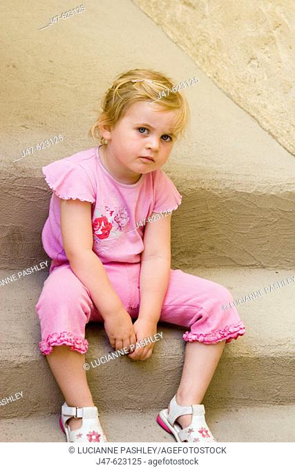 2-3 year old girl sitting on a step looking into camera, looking really miserable