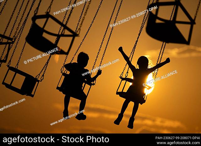 dpatop - 27 June 2023, Georgia, Batumi: Children sitting on the boardwalk in a chain carousel silhouetted against the setting sun