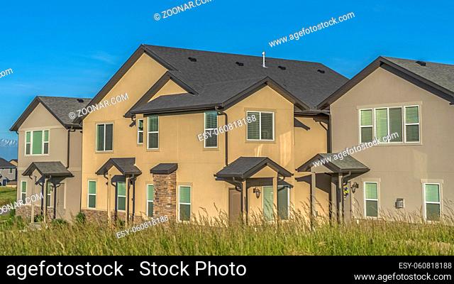 Pano frame Exterior view of multi storey homes with balconies and porticos against blue sky. Facade of houses featuring front doors with small roofs and columns