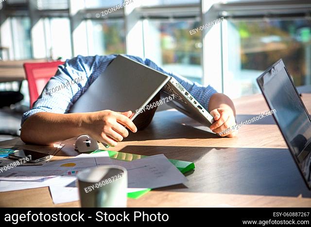 Tired businessman sleeping after hard working day in office interior. Man lying on table with laptop computer on. Business concept