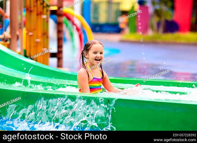 Kids play in aqua park. Children at water playground of tropical amusement park. Little girl at swimming pool. Child playing at water slide on summer vacation...