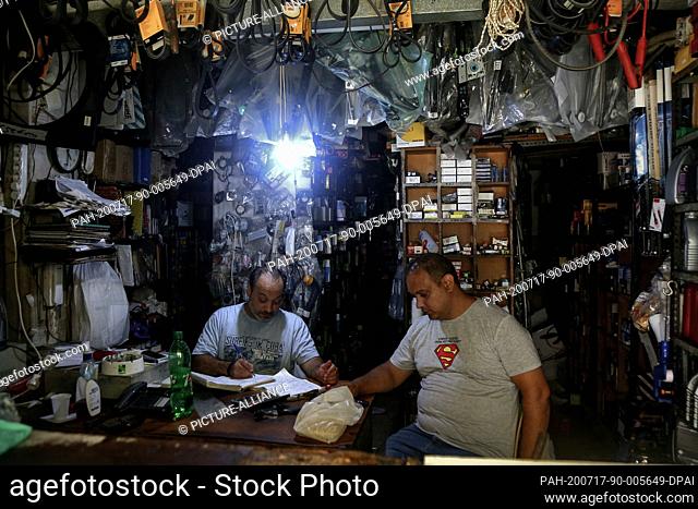 16 July 2020, Lebanon, Beirut: Two men sit inside a spare-part shop lightened with a small bulb which was taken from a nearby private generator during a...